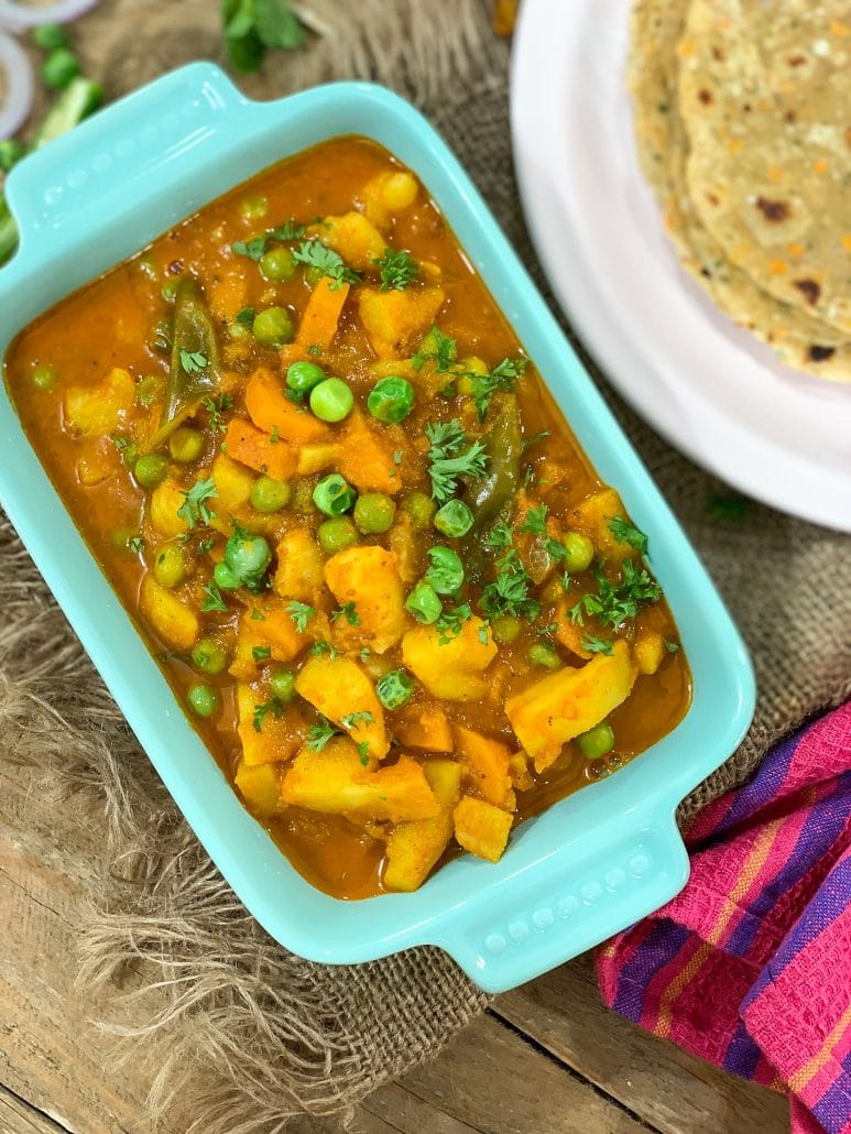 A light orange and red curry gravy, with chopped potatoes, carrots, and peas 