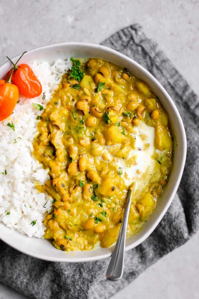 A bowl of yellow curry full of black eyed peas,  garnished with habaneros and a scoop of rice