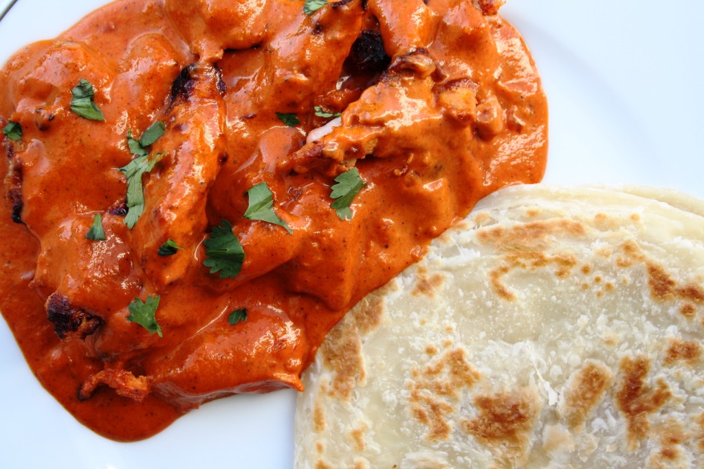 Butter chicken sitting in a bright red curry sauce with a parsley garnish