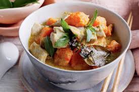 A soupy yellow curry with chunks of chicken and sweet potato, garnished with kaffir lime leaves