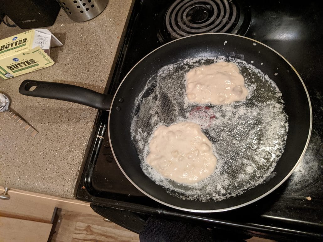2 banana fritters cooking in a skillet full of butter