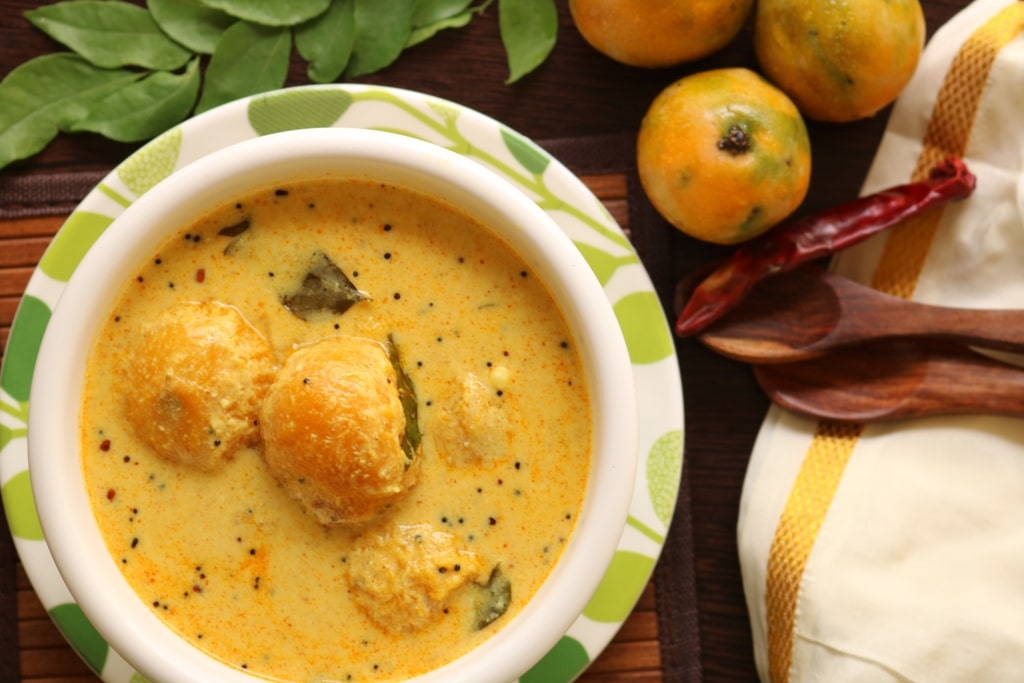 A bright yellow curry sauce with black pepper and whole mangoes