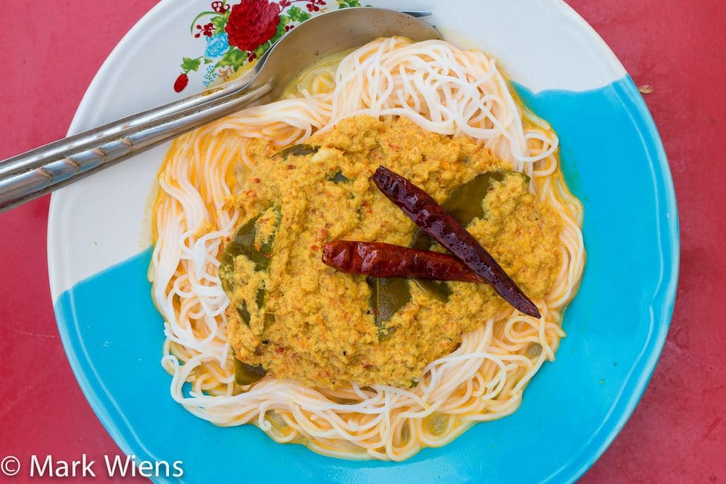 A yellow curry with red chili peppers and thin noodles