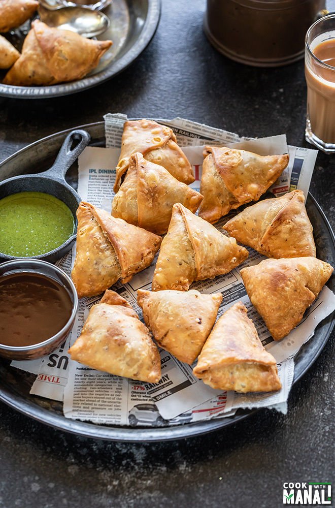 Fried samosa on top of newspaper with dipping sauces on the side