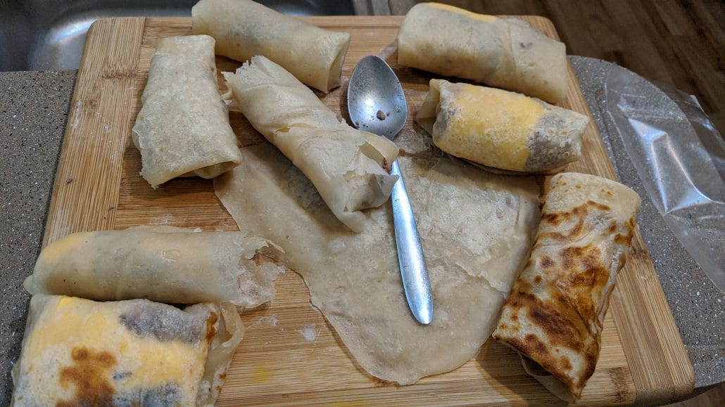 Cheeseburger spring rolls after wrapping on a cutting board