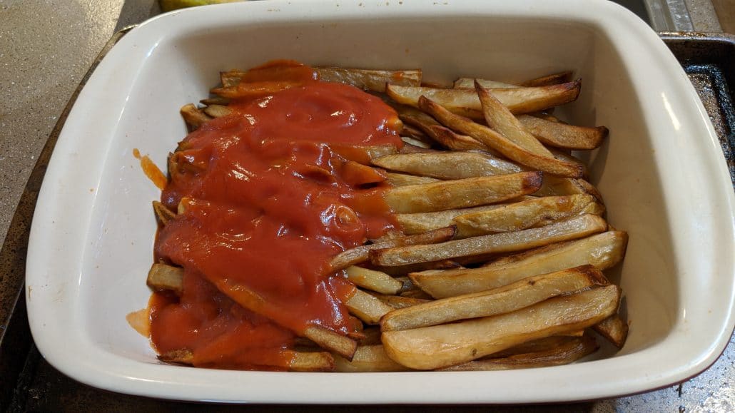 French fries covered with tomato sauce on one side of the pan