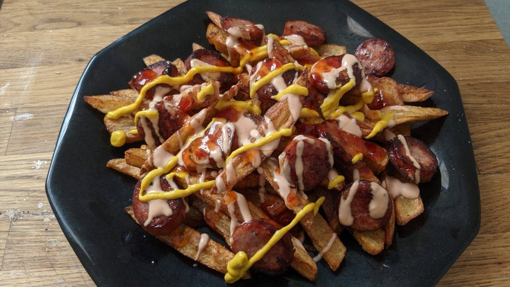 A plate of salchipapas, french fries with sausage, covered in ketchup, mayonnaise, mustard, and aji chili sauce